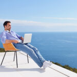Man sitting on terrace with laptop looking out to sea